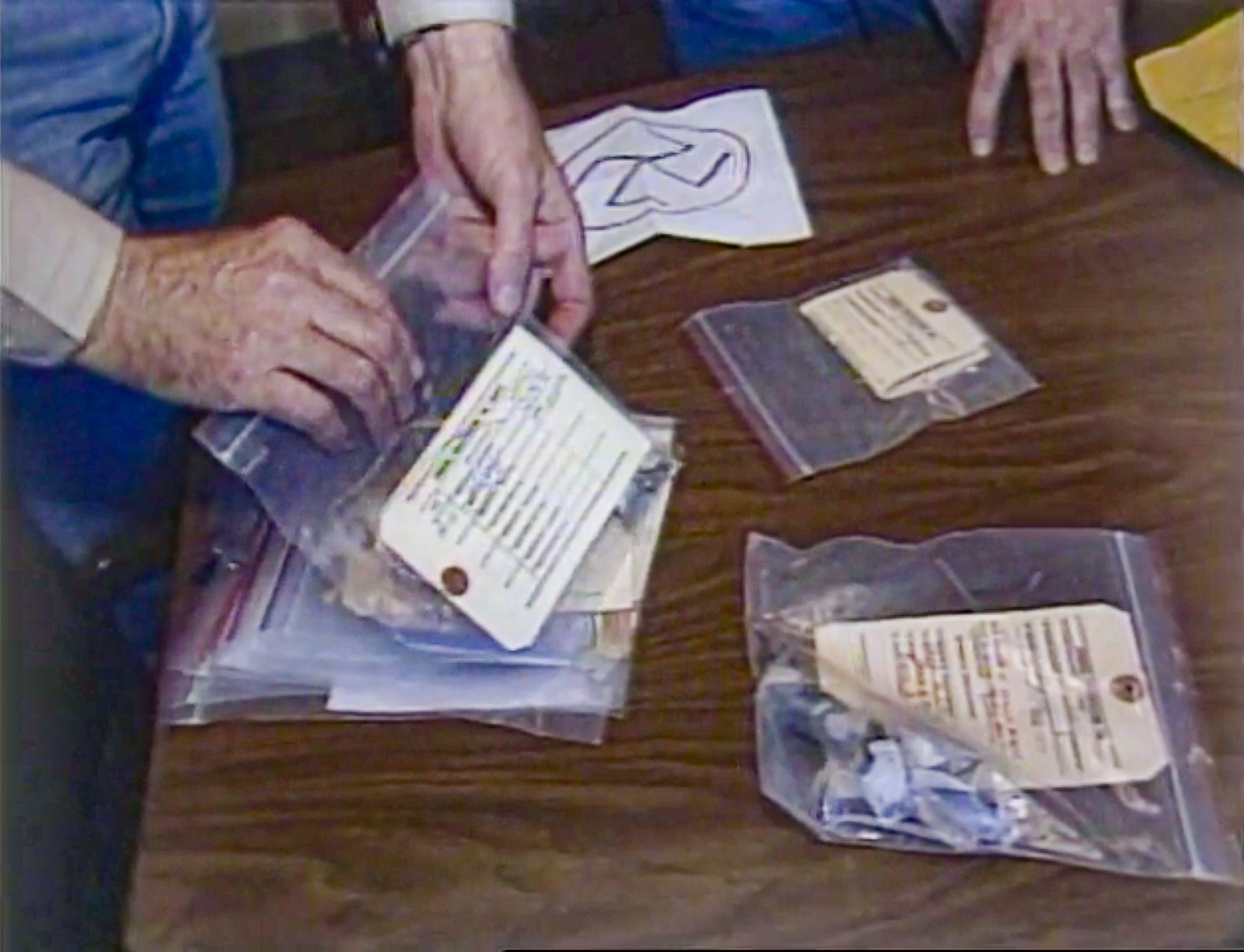 Several plastic bags full of pipe bomb fragments, with evidence tags. A note with a swastika on it sits on the table next to the plastic bags.